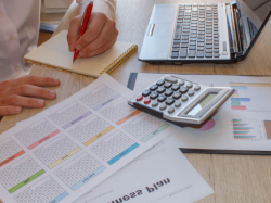 Woman doing paperwork with calculator and laptop